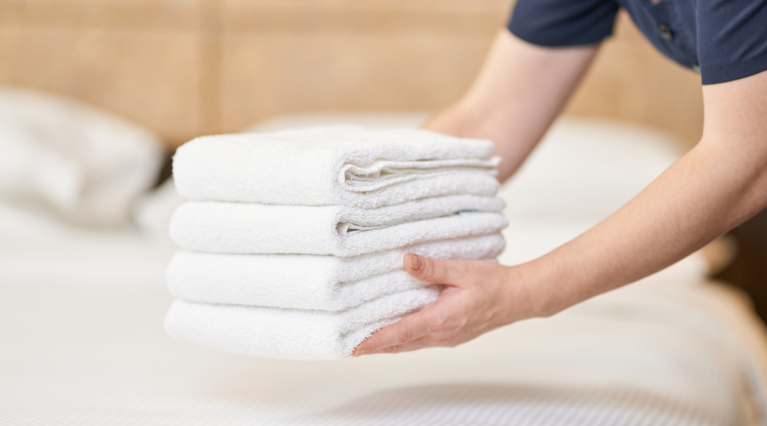 hotel laundry attendant placing towels on a bed