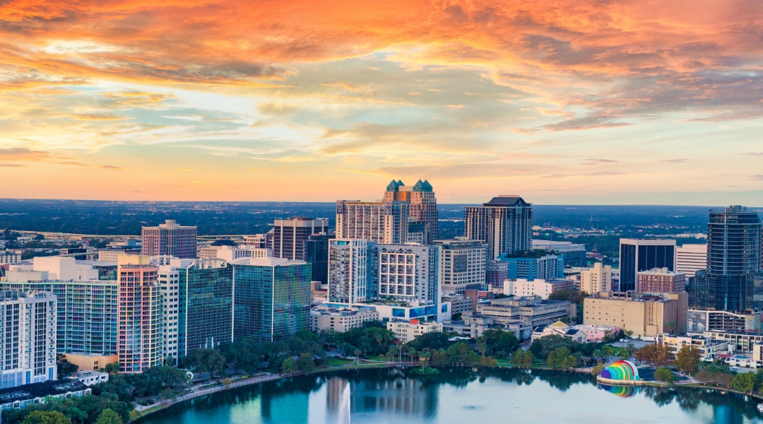 The city of Orlando, FL, under an orange and cloudy sky.